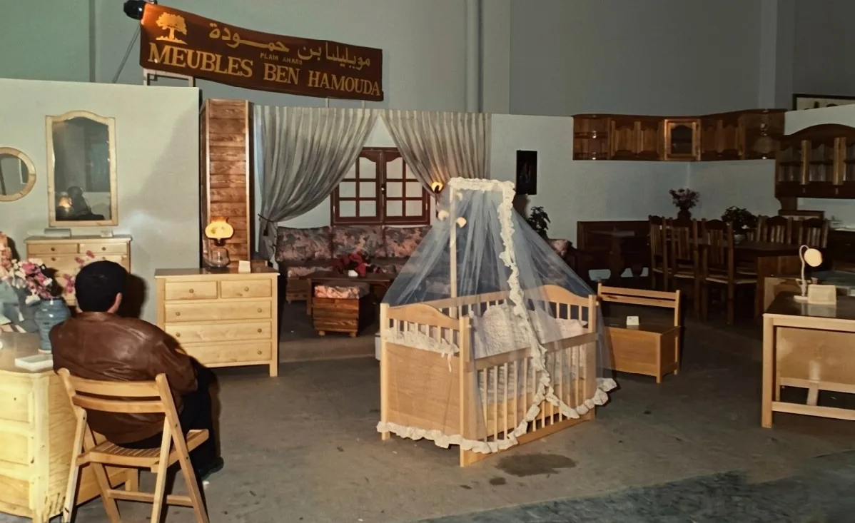 Stand Meubles Ben Hamouda sur une foire dans les années 1990 : chambre à coucher, berceau, salon et salle à manger en bois massif, sous la banderole de l'atelier